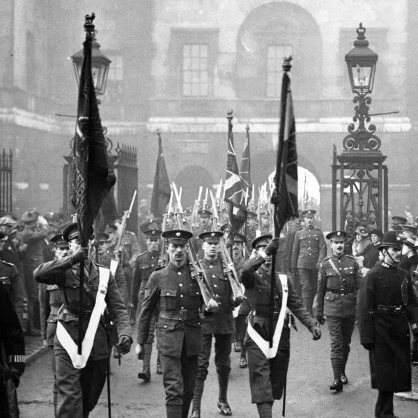 British soldiers in uniform march with flags and rifles through a gate 